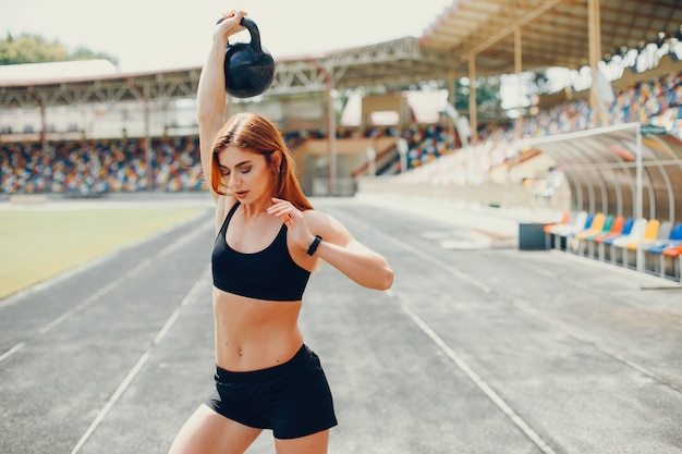 La chica en el estadio está jugando deportes.