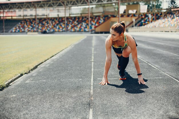 La chica en el estadio está jugando deportes.