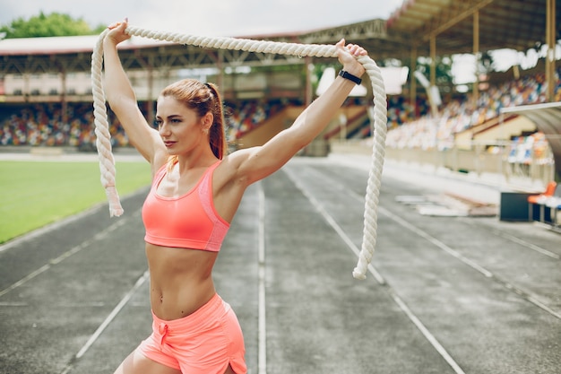 La chica en el estadio está jugando deportes.