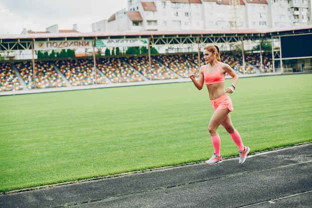 La chica en el estadio está jugando deportes.