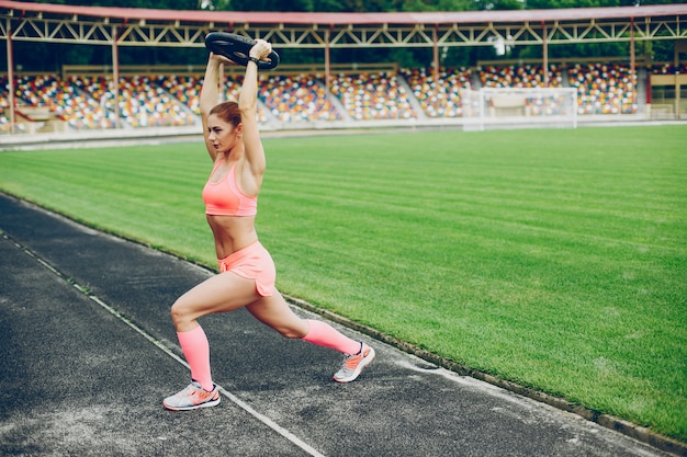 La chica en el estadio está jugando deportes.