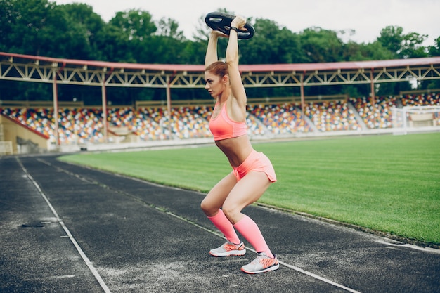 La chica en el estadio está jugando deportes.