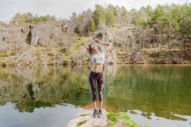 Chica estirando su cuerpo en una roca del lago