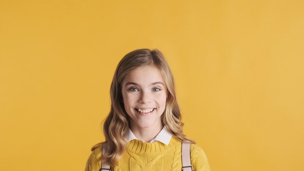 Chica estudiante adolescente bastante rubia que parece feliz de pie bajo el espacio de copia para su anuncio o contenido promocional sobre fondo amarillo. emociones felices