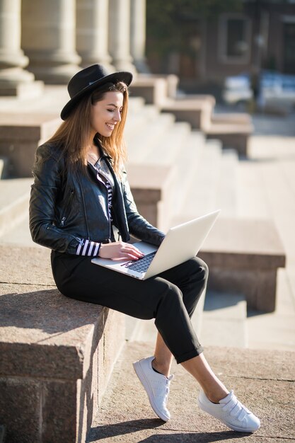 Chica estudiante alegre joven empresaria trabaja con su computadora portátil de marca en el centro de la ciudad