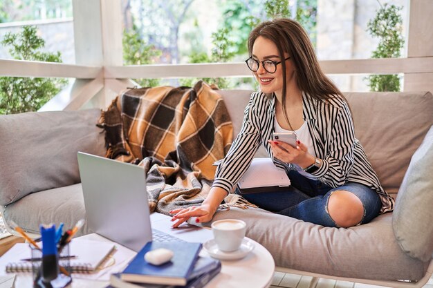 Chica estudiante bastante aprendiendo en casa con ordenador portátil y teléfono móvil.