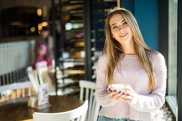 Chica estudiante bastante joven modelo vestida con ropa casual jeans en café tiene taza de té de café en sus manos