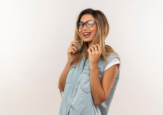 Chica estudiante bonita joven alegre con gafas y bolsa trasera con auriculares en el cuello sosteniendo auriculares aislados en blanco