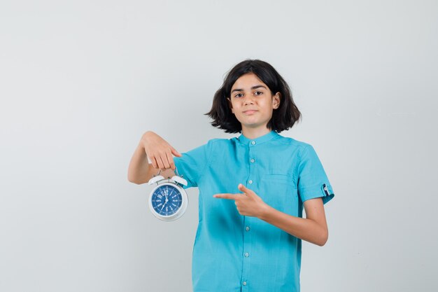 Chica estudiante en camisa azul apuntando al reloj y mirando seguro