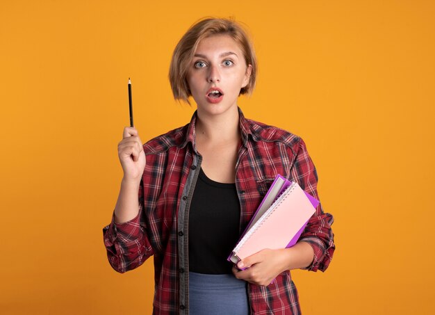 Chica estudiante eslava joven sorprendida sostiene cuaderno y libro de lápiz