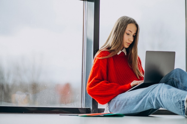 Chica estudiante estudiando en la computadora junto a la ventana