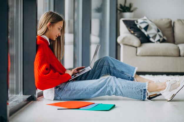 Chica estudiante estudiando en la computadora junto a la ventana