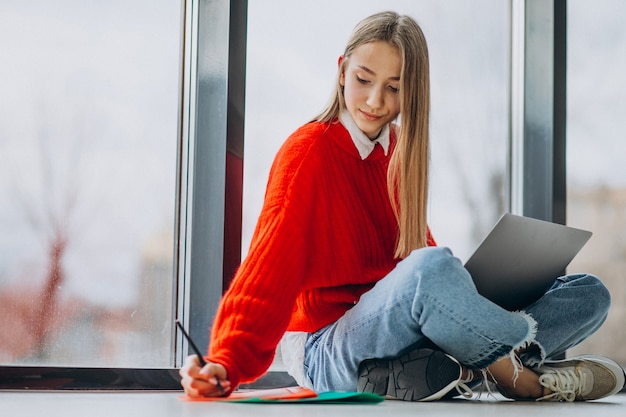 Chica estudiante estudiando en la computadora junto a la ventana