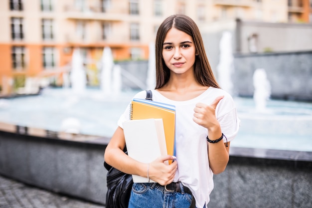 Chica estudiante feliz posando con los pulgares arriba mirándote en la calle