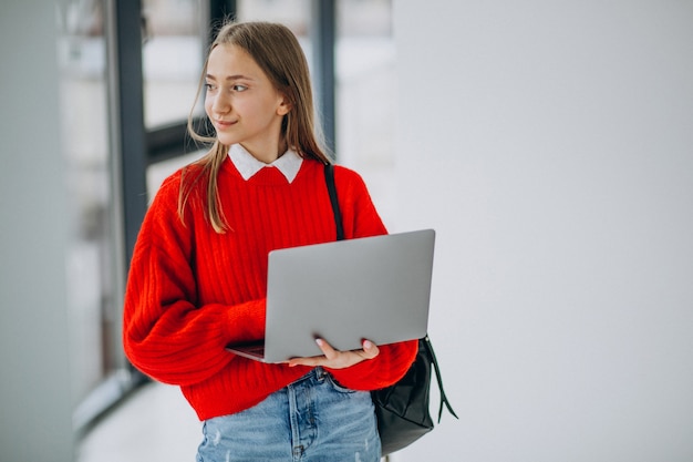 Chica estudiante con laptop de pie junto a la ventana en el pasillo