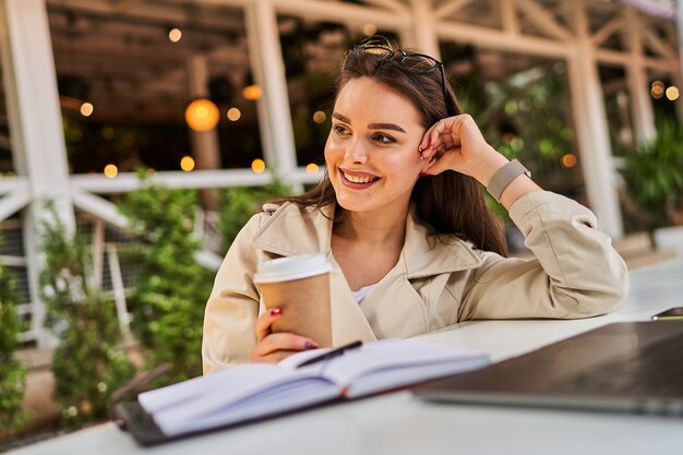 Chica estudiante que aprende en línea al aire libre con café para llevar.