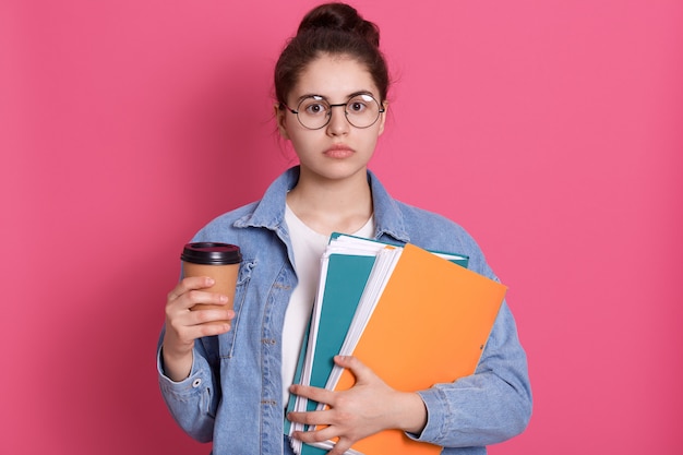 Chica estudiante seria con carpeta de papel y llevar café en manos