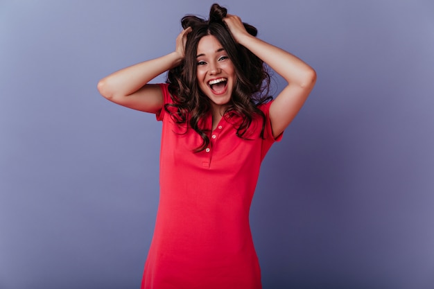 Chica europea inspirada riendo y jugando con su cabello ondulado. foto de dama blanca emocionada aislada en la pared púrpura con una sonrisa.