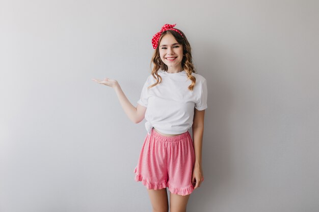 Chica europea interesada en ropa de dormir divirtiéndose. Señora blanca refinada en pantalones cortos rosas posando con una sonrisa encantadora.