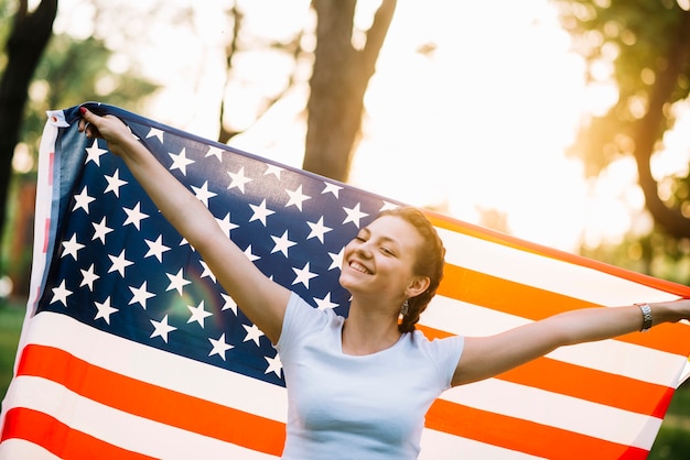 Chica feliz con bandera americana en la naturaleza