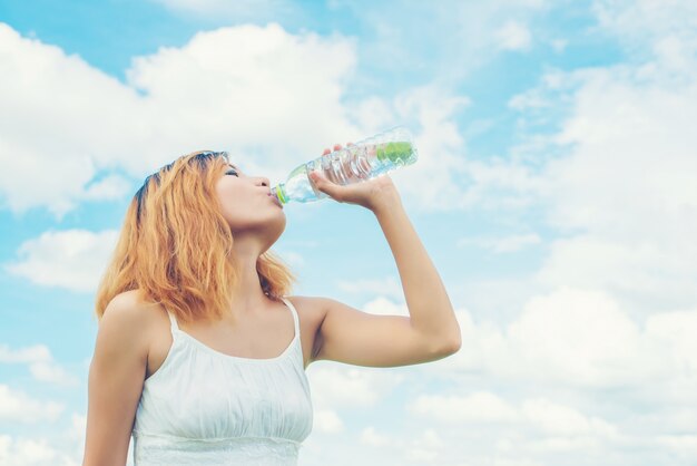 Chica feliz bebiendo agua con el cielo de fondo