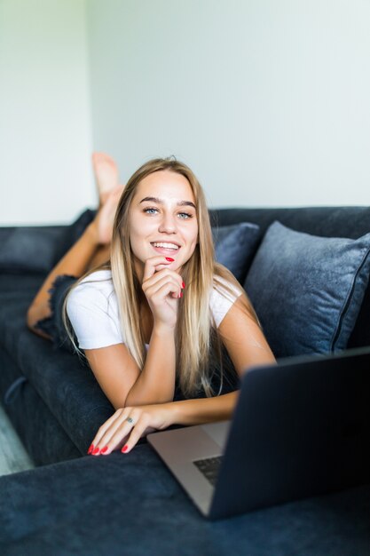 Chica feliz chateando en línea en la computadora portátil. Sonriente mujer rubia mensajes con amigos en la computadora. Concepto de redes sociales, comunicación y tecnología.