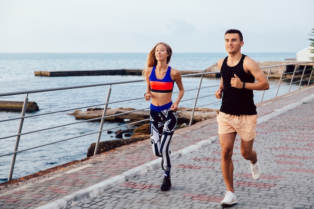 Chica feliz y chico corriendo juntos en el muelle cerca del mar. Concepto del deporte