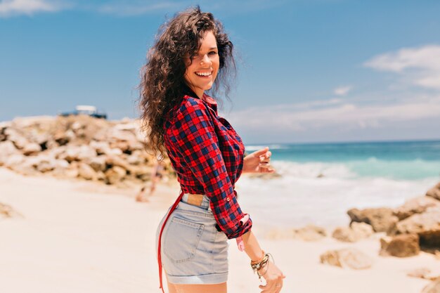 Chica feliz emocionada con pantalones cortos y camiseta en la orilla del mar en la playa de arena