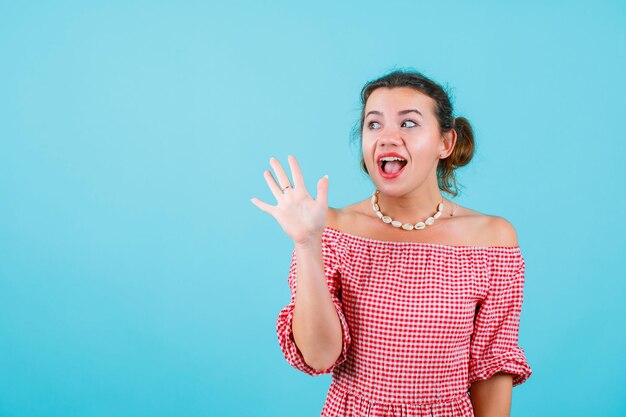 La chica feliz está mirando hacia arriba mostrando un gesto de hola con la mano en el fondo azul