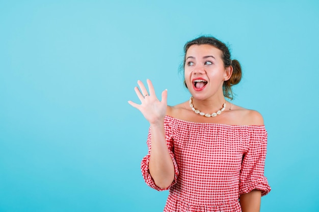 La chica feliz está mirando hacia arriba mostrando un gesto de hola con la mano en el fondo azul