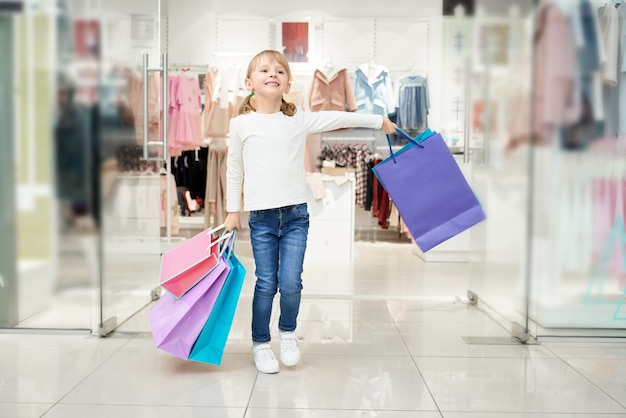 Chica feliz posando en el centro comercial con muchas bolsas.