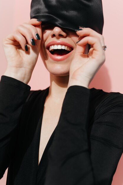 Una chica feliz posando con un moderno pañuelo negro en la cabeza Foto de estudio de una modelo femenina positiva en turbante riéndose sobre fondo rosa