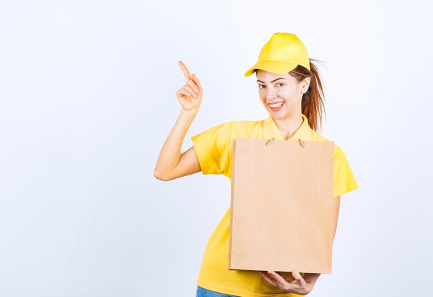 Chica femenina en uniforme amarillo sosteniendo una bolsa de cartón y apuntando a algún lugar.