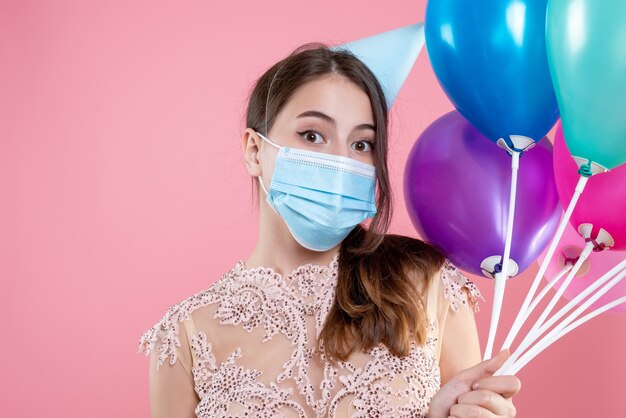 Chica de fiesta de vista frontal de primer plano con corona y máscara sosteniendo globos