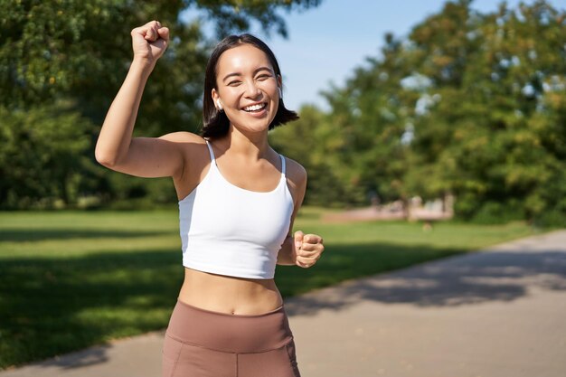 Chica fitness feliz lograr meta terminar maratón corriendo con las manos arriba celebrando la victoria mientras jogg