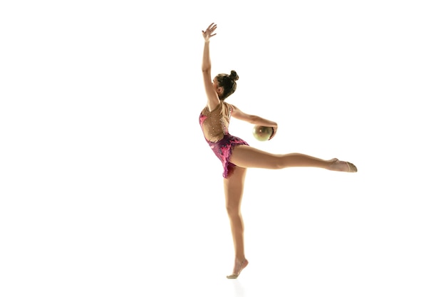 Chica flexible joven aislada en la pared blanca. Modelo femenino adolescente como artista de gimnasia rítmica practicando con equipo. Ejercicios de flexibilidad, equilibrio. Gracia en movimiento, deporte.