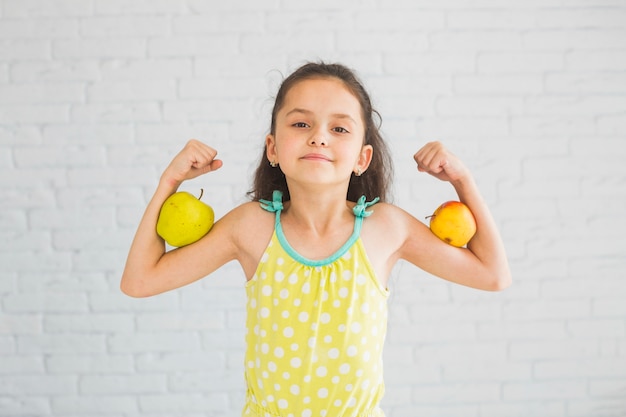 Foto gratuita chica flexionando sus manos sosteniendo la manzana en su bíceps