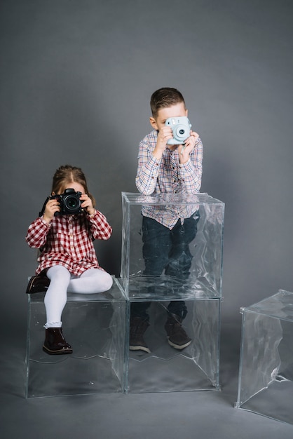 Foto gratuita chica fotografiando con cámara y niño fotografiando con cámara instantánea vintage