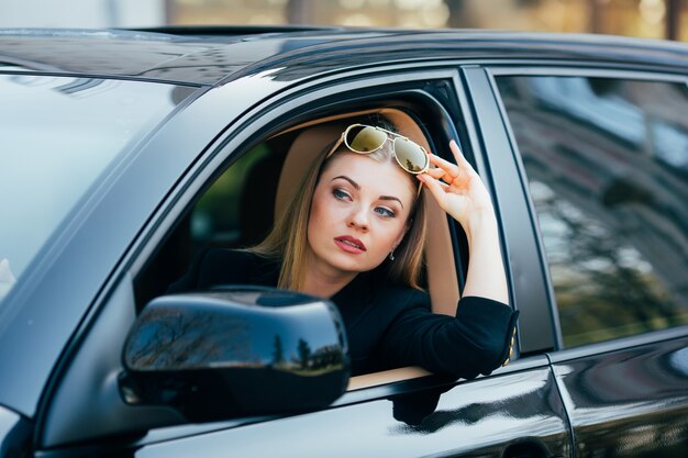 Chica con gafas de sol conduce un coche y mira desde la ventana