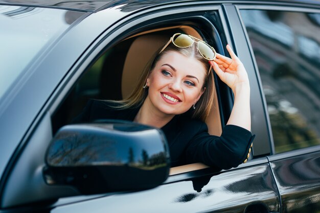 Chica con gafas de sol conduce un coche y mira desde la ventana