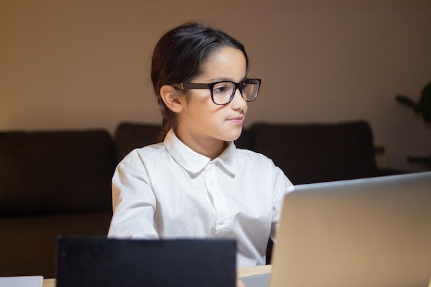 Chica geek concentrada en gafas programando usando laptop. Colegiala creando una nueva aplicación para la escuela. Educación, concepto de hobby