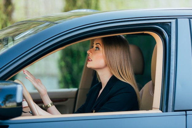 Chica gesto enojado mira en el espejo trasero en el coche trasero