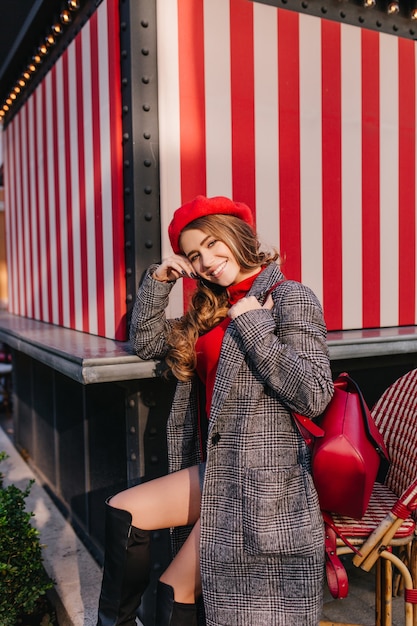 Chica glamorosa en abrigo de tweed de moda sentado en la calle con bonita sonrisa