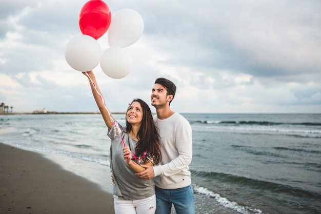 Chica con globos mientras su novio la agarra de la mano con el mar de fondo