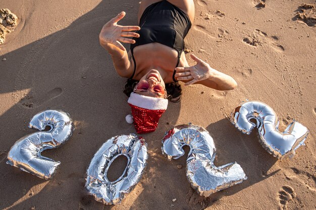 Chica con globos plateados en forma de números para el próximo año cerca del mar