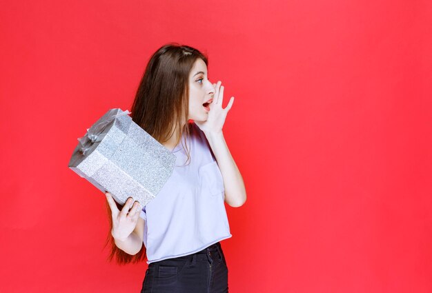 Foto gratuita chica gritando y llamando a alguien para recibir la caja de regalo plateada.