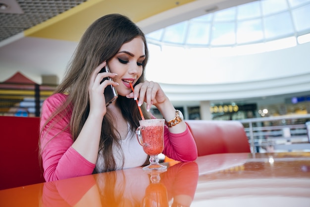 Chica guapa bebiendo mientras habla por teléfono