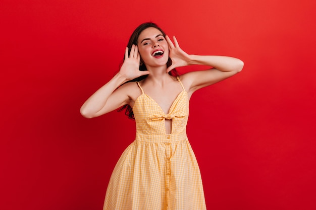 Chica guapa de buen humor grita en voz alta. Retrato de dama con lápiz labial rojo en vestido de verano a cuadros en pared brillante aislada.