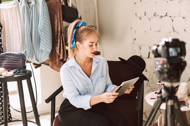 Chica guapa con camisa azul soñando usando la tableta mientras graba un nuevo video de moda para vlog