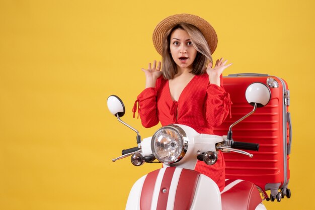 Chica guapa en ciclomotor con maleta roja confusa